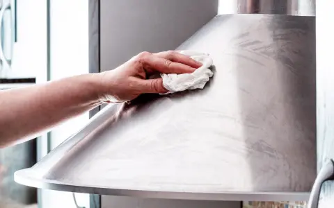 Hand poliert mit einem Tuch eine Dunstabzugshaube aus Edelstahl, um sie zum Glänzen zu bringen.