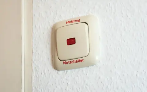Ein beiger Schalter an einer weißen Wand mit der Aufschrift "Heizung" und "Notschalter". Dieser heizungsnotschalter pflicht ist wichtig für die Sicherheit.