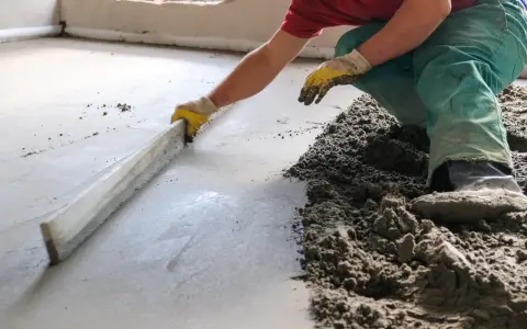 Mann verlegt Estrich mit einer Richtlatte.