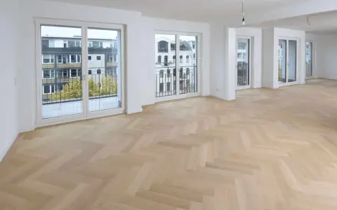 Ein heller Fischgrätenparkettboden, frisch nach dem Parkett schleifen, erstrahlt in einem modernen Wohnraum mit großen Fenstern und Balkonen.