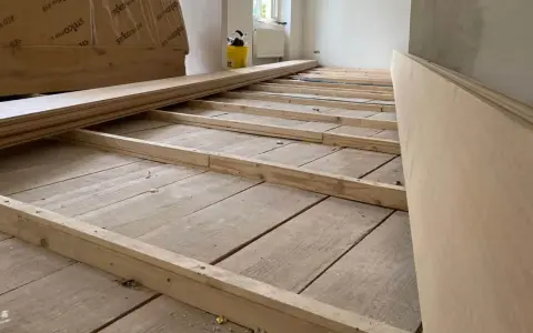 Holzbalken werden auf einem alten Holzboden verlegt, um ihn für eine neue Verkleidung vorzubereiten. So kann man den Boden ausgleichen ohne Ausgleichsmasse.