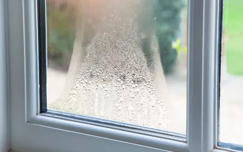 Fenster beschlagen von innen. Kleine Wassertropfen bilden ein Muster auf der Scheibe, das den Blick nach draußen verschwimmen lässt.