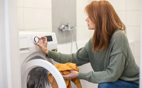 Frau stellt Waschmaschine ein, achtet auf wasserverbrauch. Sie hält ein gelbes Kleidungsstück.