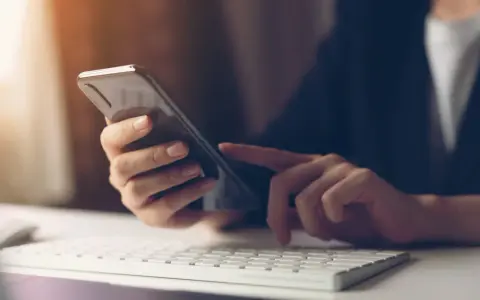 Person tippt auf Smartphone, weil hey Google funktioniert nicht. Tastatur und Maus im Vordergrund.