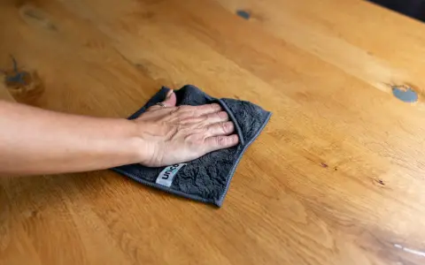 Hand wischt mit Tuch über Holzoberfläche, um Wasserflecken zu entfernen.