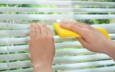 Hände reinigen mit gelbem Tuch die Lamellen einer Jalousie.