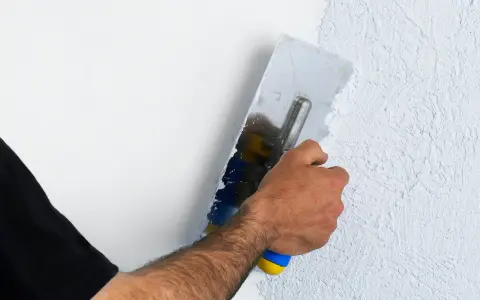 Hand mit Glättekelle bearbeitet eine Wand, um den Putz zu filzen und eine strukturierte Oberfläche zu schaffen.