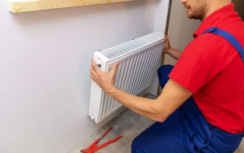 Handwerker montiert Heizkörper. Werkzeug liegt bereit.