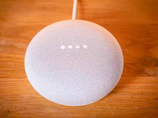 Ein weißer Google Nest Mini auf einem Holztisch. Die vier Lichter zeigen an, dass das Gerät auf Werkseinstellung zurückgesetzt wird.