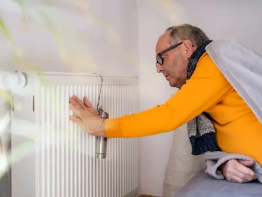 Mann prüft Heizung. Kein warmwasser und heizung wie lange zumutbar? Er ist in Decke gehüllt.