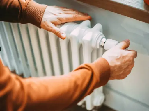 Hände stellen Heizung ein. Der Heizwert von Erdgas sorgt für wohlige Wärme im Haus.