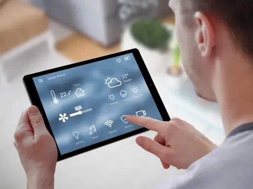 Mann steuert Smart Home per Tablet. Temperatur, Wetter & Lüftung sind sichtbar. Über Bluetooth vernetzt.