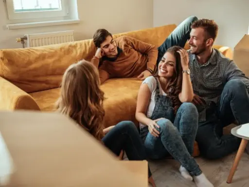 Glückliche Freunde lachen auf dem Boden vor einem Sofa, umgeben von Umzugskartons. Ein privater Vermieter könnte ihnen hier beim Einzug helfen.