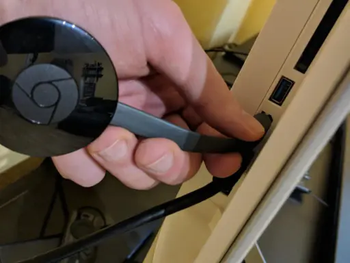 Hand connects a black Chromecast to a USB port on a device, preparing to chromecast mit wlan verbinden.