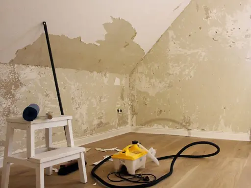 Raufasertapete entfernen: Dampfreiniger und Werkzeug auf dem Boden, die Wand ist teilweise abgerissen.