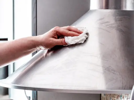 Hand poliert mit einem Tuch eine Dunstabzugshaube aus Edelstahl, um sie zum Glänzen zu bringen.