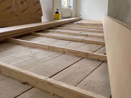 Holzbalken werden auf einem alten Holzboden verlegt, um ihn für eine neue Verkleidung vorzubereiten. So kann man den Boden ausgleichen ohne Ausgleichsmasse.
