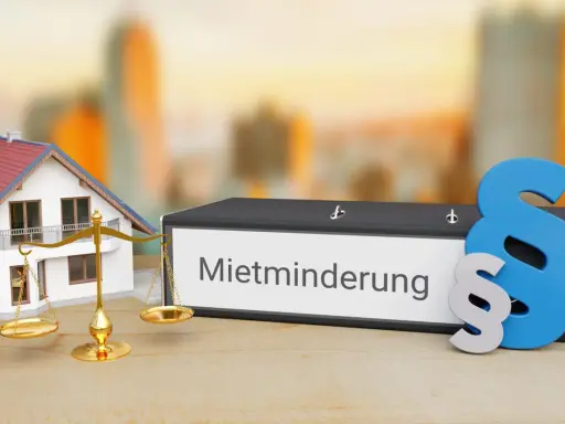 Hausmodell, Waage und Ordner mit "Mietminderung" Schriftzug. Ein Paragrafensymbol deutet auf rechtliche Aspekte hin, z.B. bei Problemen mit der Heizung.