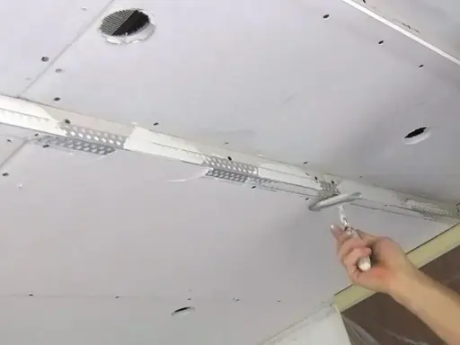 Hand spachtelt Rigips Fugen mit einem Spachtel. Der Deckenbau schreitet voran.