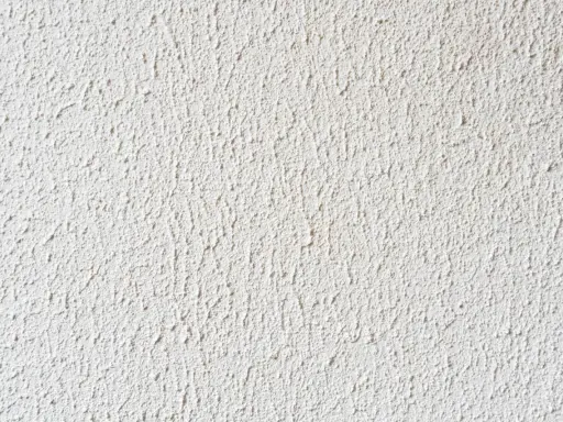 Eine weiße Wand mit feinem Rollputz auf Tapete. Die Struktur ist unregelmäßig und erzeugt ein lebendiges Oberflächenbild.