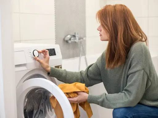 Frau stellt Waschmaschine ein, achtet auf wasserverbrauch. Sie hält ein gelbes Kleidungsstück.