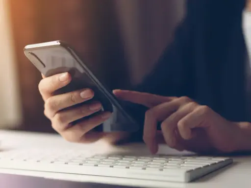 Person tippt auf Smartphone, weil hey Google funktioniert nicht. Tastatur und Maus im Vordergrund.