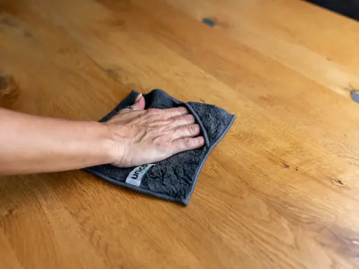 Hand wischt mit Tuch über Holzoberfläche, um Wasserflecken zu entfernen.