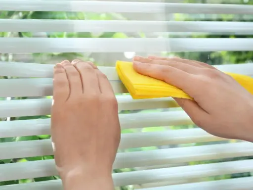 Hände reinigen mit gelbem Tuch die Lamellen einer Jalousie.