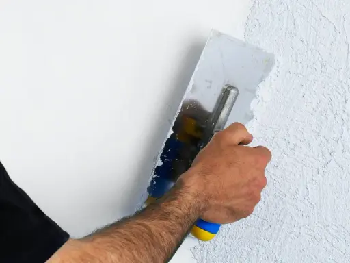 Hand mit Glättekelle bearbeitet eine Wand, um den Putz zu filzen und eine strukturierte Oberfläche zu schaffen.