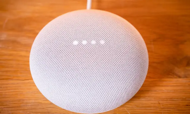 Ein weißer Google Nest Mini auf einem Holztisch. Die vier Lichter zeigen an, dass das Gerät auf Werkseinstellung zurückgesetzt wird.