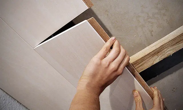 Hände bringen Deckenpaneele an, ohne Unterkonstruktion. Die Paneele werden direkt an die Decke geklebt oder geschraubt.