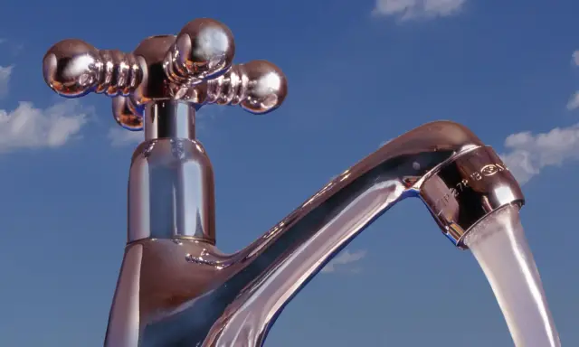 Chromhahn mit laufendem Wasser vor blauem Himmel. Der Wasserdruck ist gut, die **druck wasserleitung** liefert kräftig.