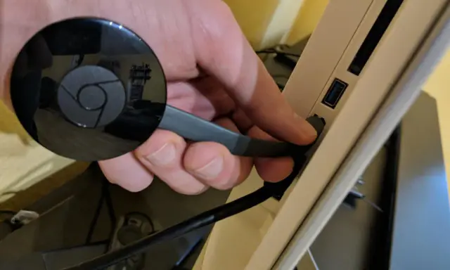 Hand connects a black Chromecast to a USB port on a device, preparing to chromecast mit wlan verbinden.