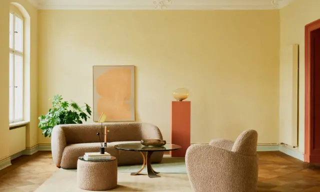 Ein Wohnzimmer mit gelben Wänden und einer grünen Decke, die frisch gestrichen wurde. Gemütliche Bouclé-Möbel und ein runder Couchtisch laden zum Verweilen ein.
