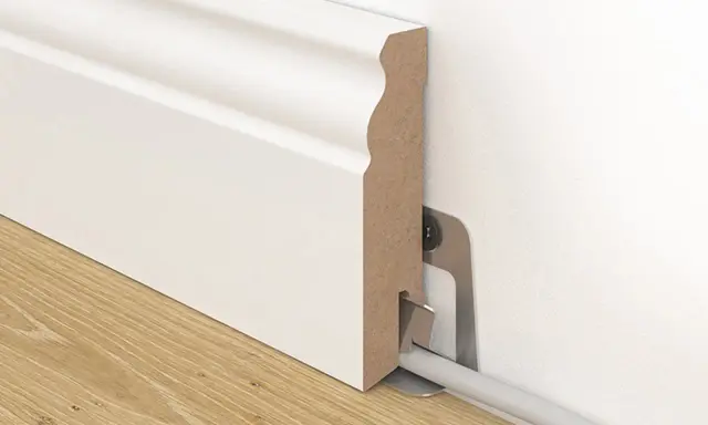 Weiße Sockelleiste mit Kabelkanal, die an der Wand befestigt ist. So kann man Leisten kleben und Kabel verstecken.