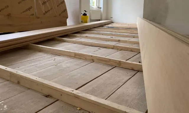 Holzbalken werden auf einem alten Holzboden verlegt, um ihn für eine neue Verkleidung vorzubereiten. So kann man den Boden ausgleichen ohne Ausgleichsmasse.