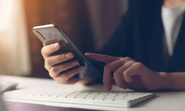 Person tippt auf Smartphone, weil hey Google funktioniert nicht. Tastatur und Maus im Vordergrund.