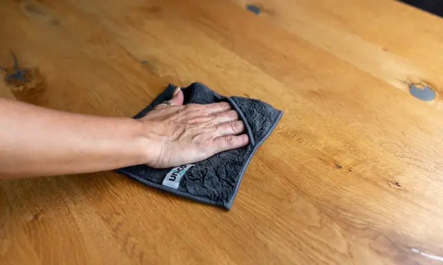Hand wischt mit Tuch über Holzoberfläche, um Wasserflecken zu entfernen.