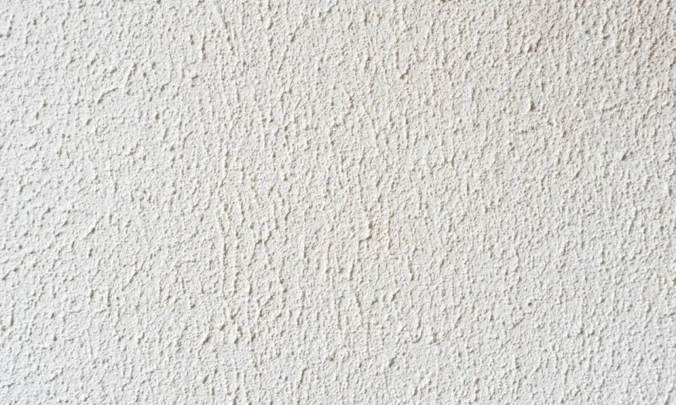 Eine weiße Wand mit feinem Rollputz auf Tapete. Die Struktur ist unregelmäßig und erzeugt ein lebendiges Oberflächenbild.