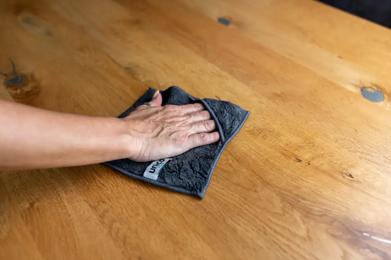 Hand wischt mit Tuch &uuml;ber Holzoberfl&auml;che, um Wasserflecken zu entfernen.