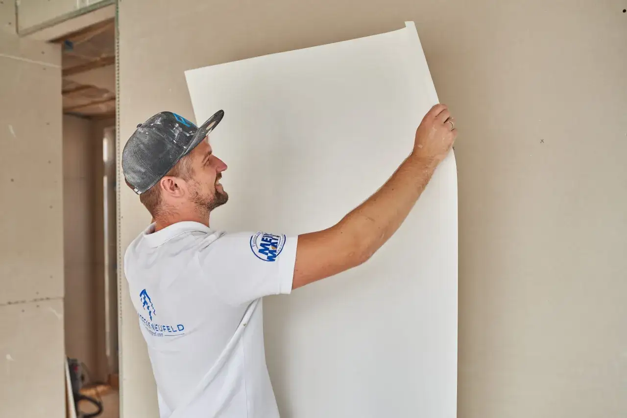 Maler tapeziert Malervlies an einer Wand.