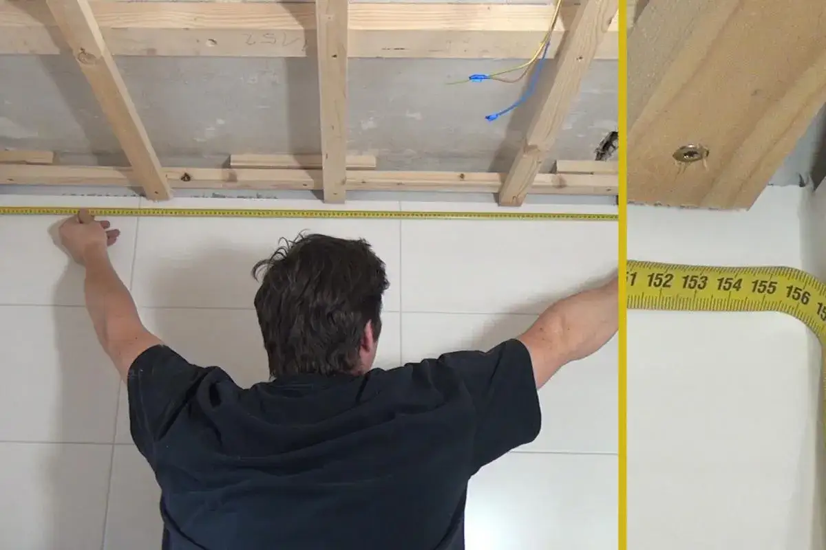 Mann misst die Decke f&uuml;r das Anbringen von Deckenpaneelen ohne Unterkonstruktion. Holzbalken sind sichtbar.