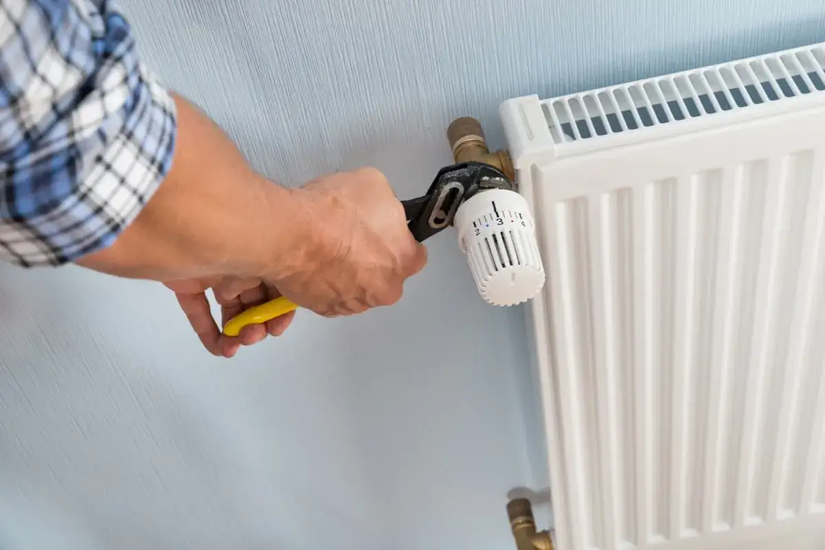 Hand mit Rohrzange dreht am Heizk&ouml;rperthermostat, um ihn abzuschrauben.