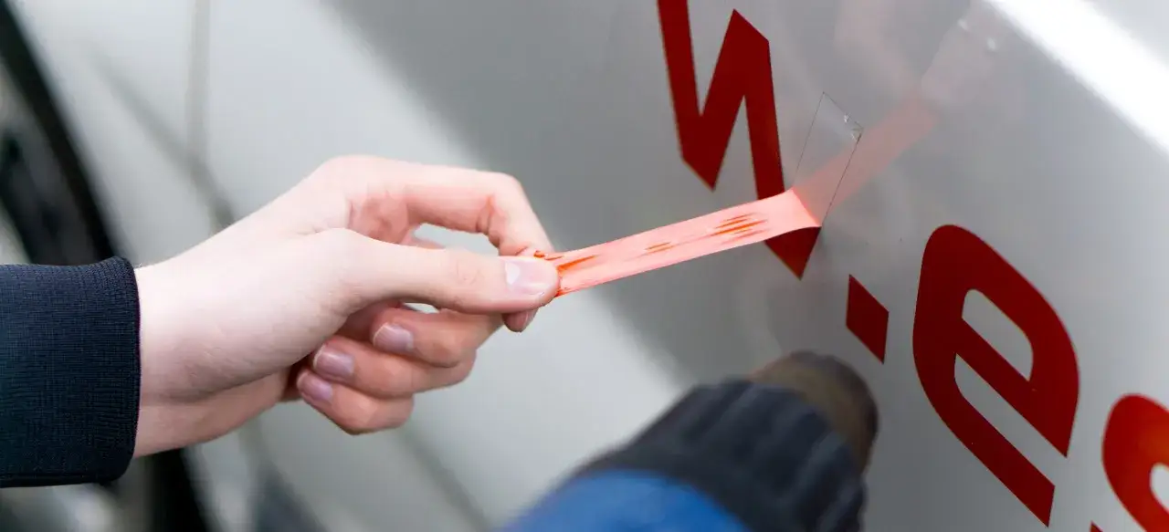 Hand entfernt mit Heißluftföhn klebeetiketten von einem Fahrzeug.