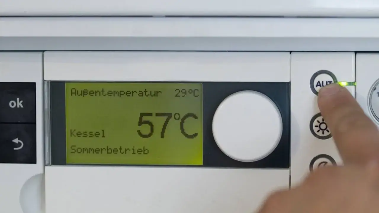 Display zeigt Außentemperatur 29°C, Kessel 57°C, Sommerbetrieb. Finger drückt auf