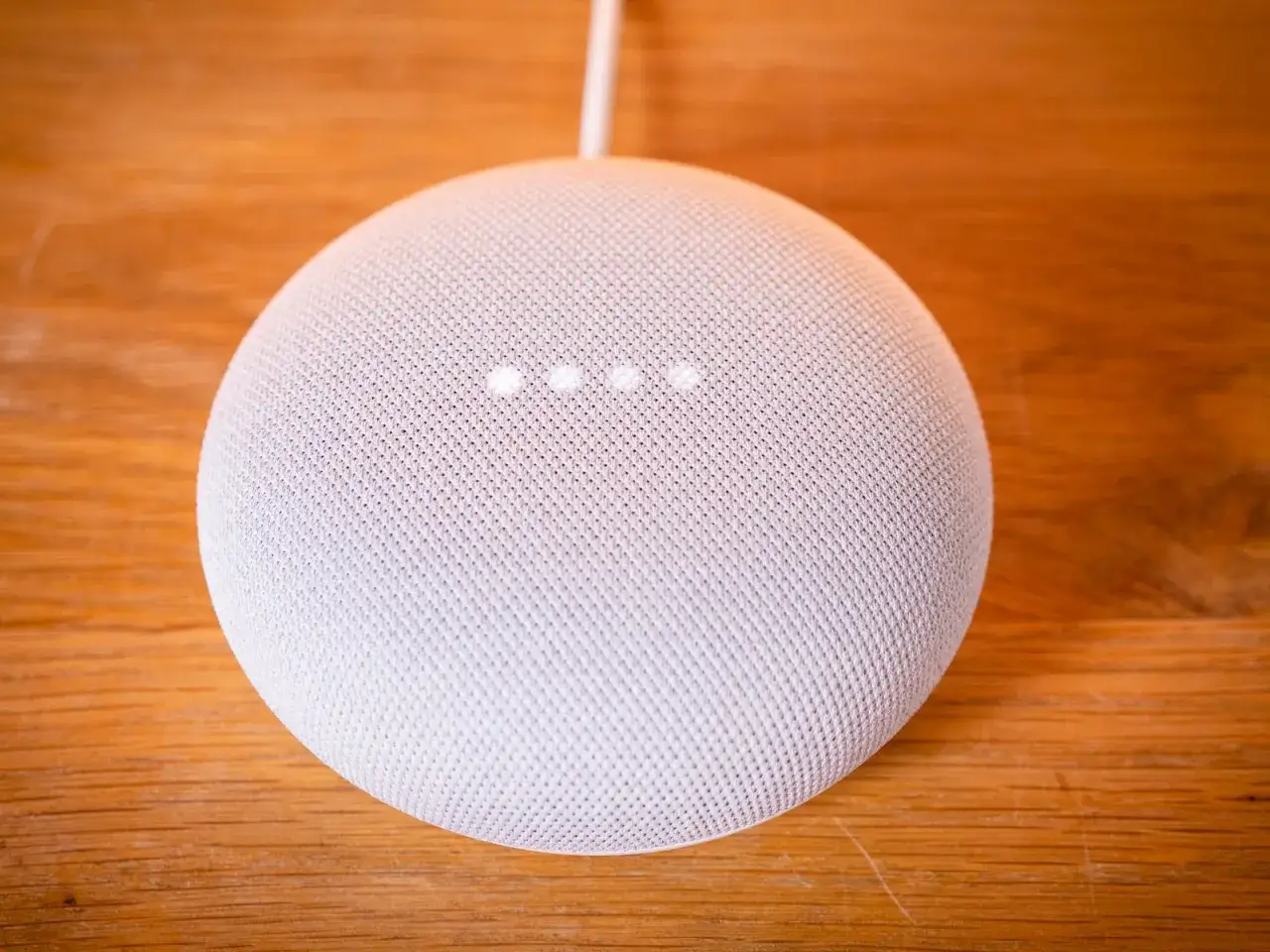 Ein weißer Google Nest Mini auf einem Holztisch. Die vier Lichter zeigen an, dass das Gerät auf Werkseinstellung zurückgesetzt wird.
