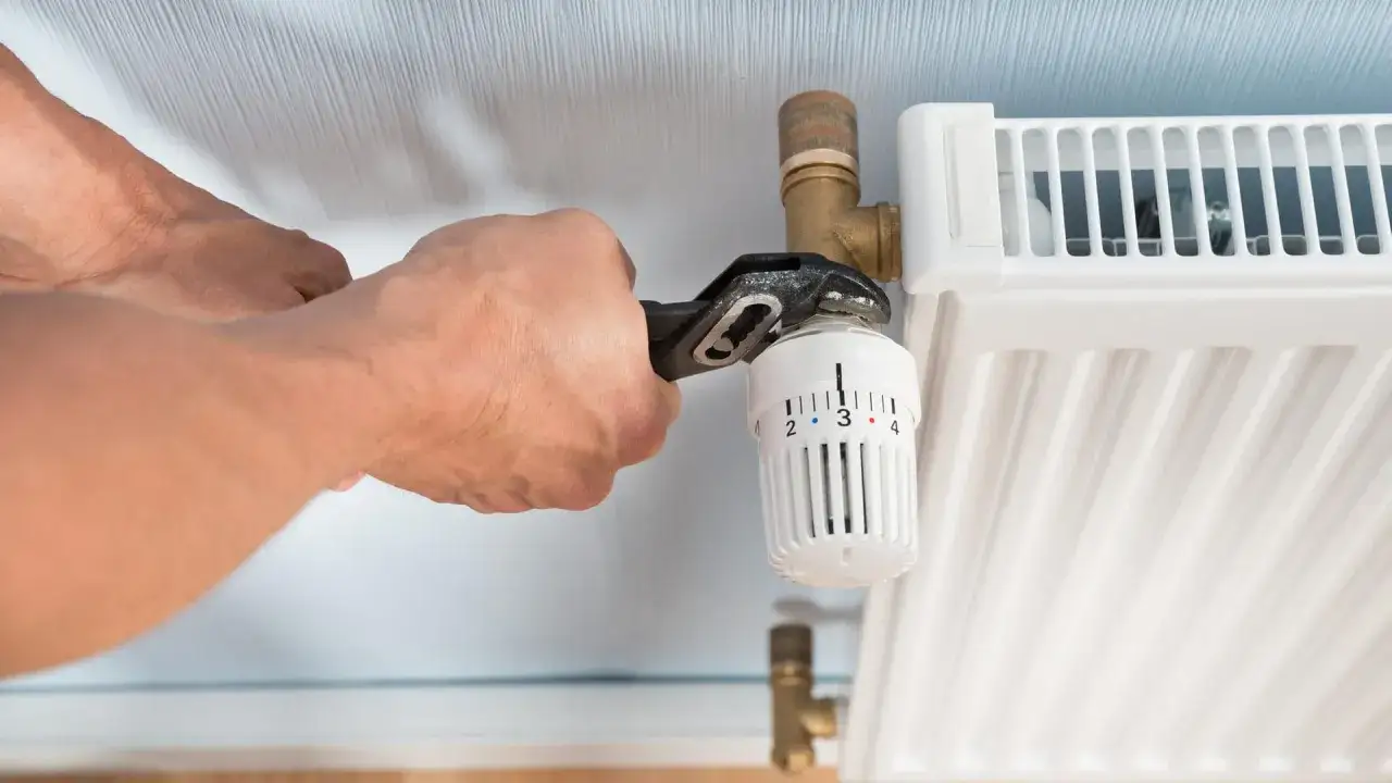 Hände mit Zange am Thermostatventil, um die Heizung abmontieren.