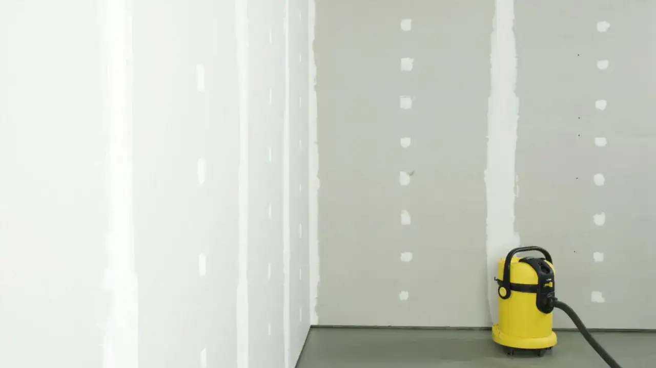 Ecke eines Raumes mit frisch gespachtelten Rigips-Fugen. Ein gelber Industriesauger steht bereit, um den Staub beim Schleifen aufzufangen.