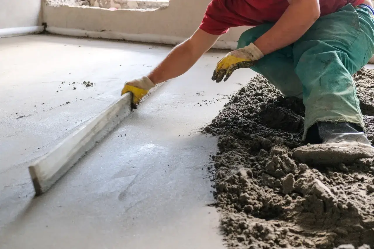 Hand mit Handschuh glättet frischen Estrich mit Richtscheit.
