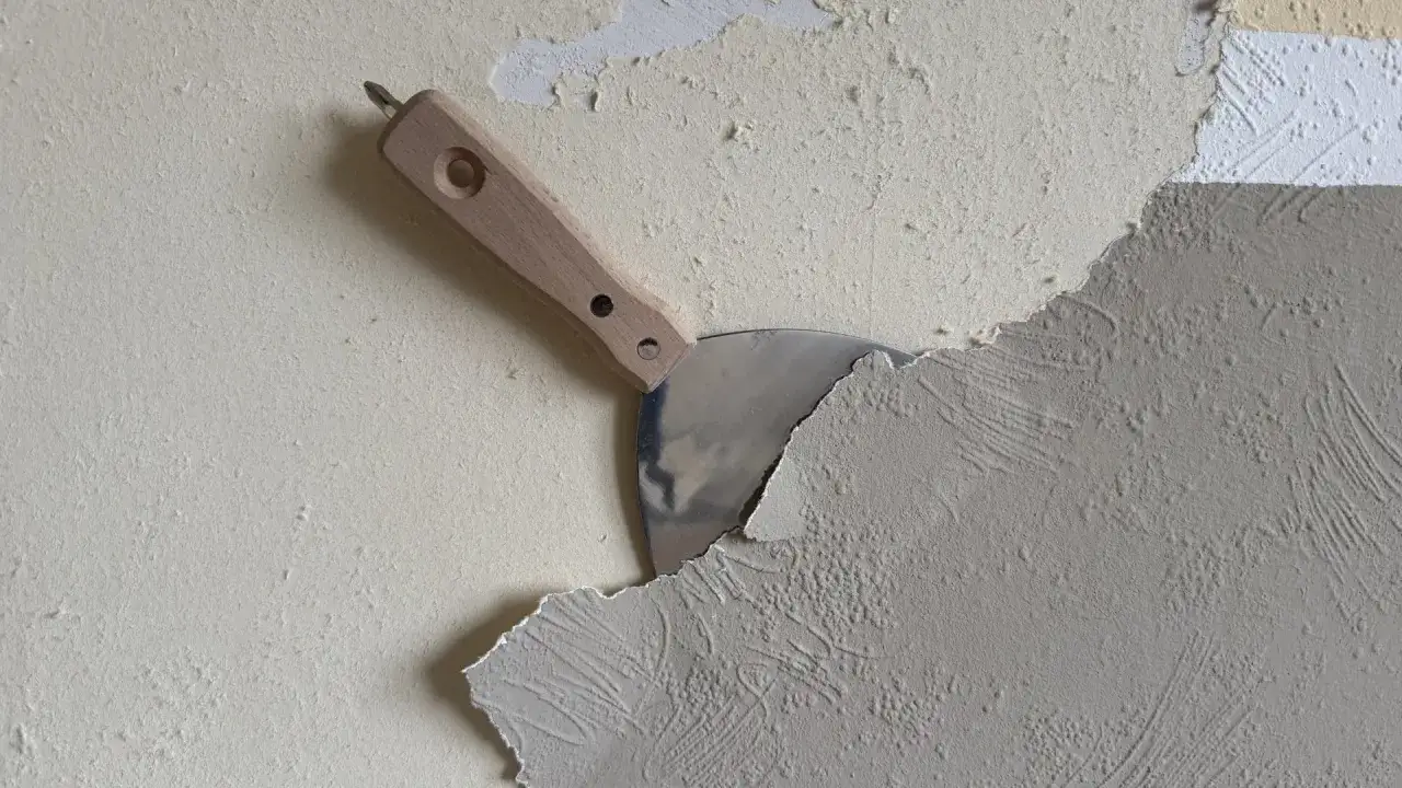 Spachtel löst grobe Vliestapete von der Wand. Die Arbeit, Vliestapete entfernen, ist im Gange.